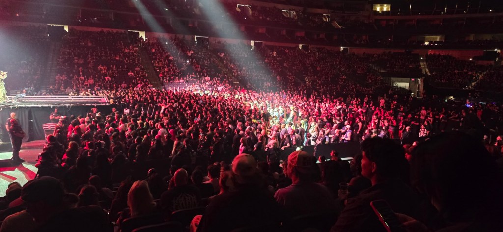 A large crowd gathered in a concert venue, illuminated by stage lights, enjoying a performance.