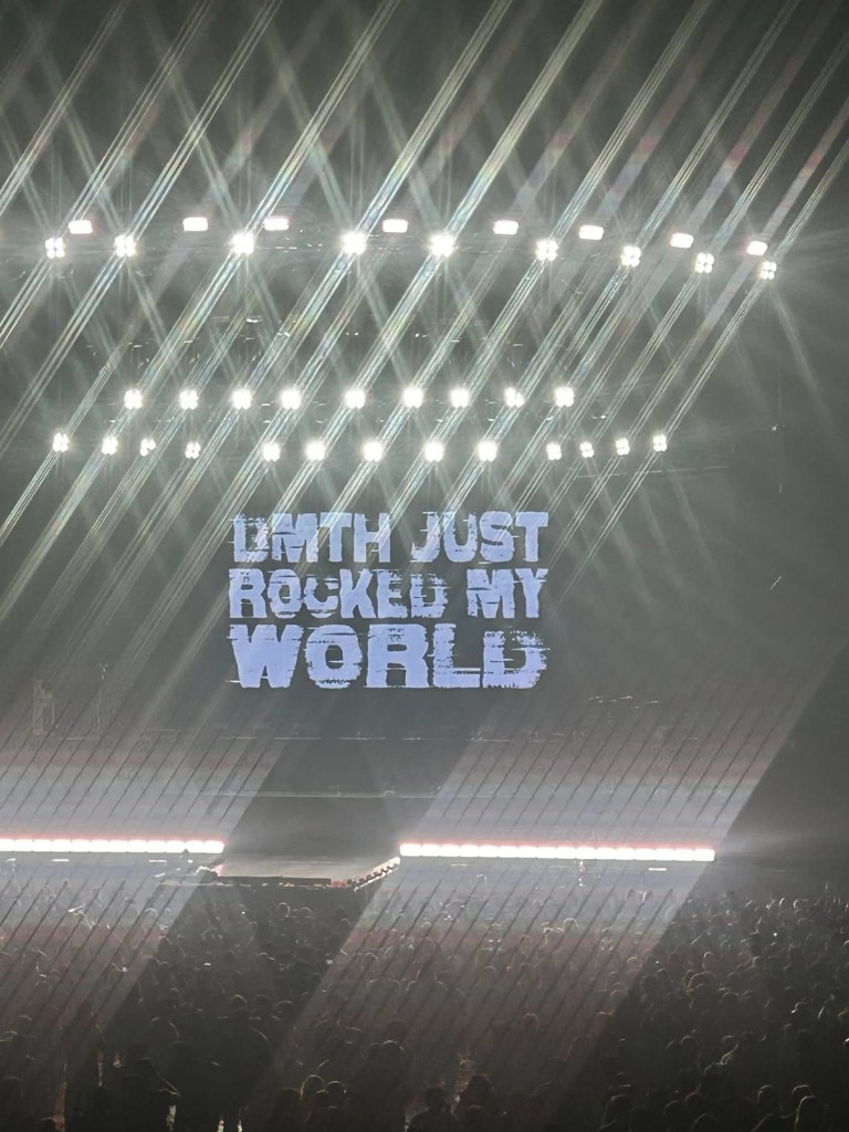 A concert stage with bright lights and the words 'LMTH JUST ROCKED MY WORLD' displayed prominently in bold letters.